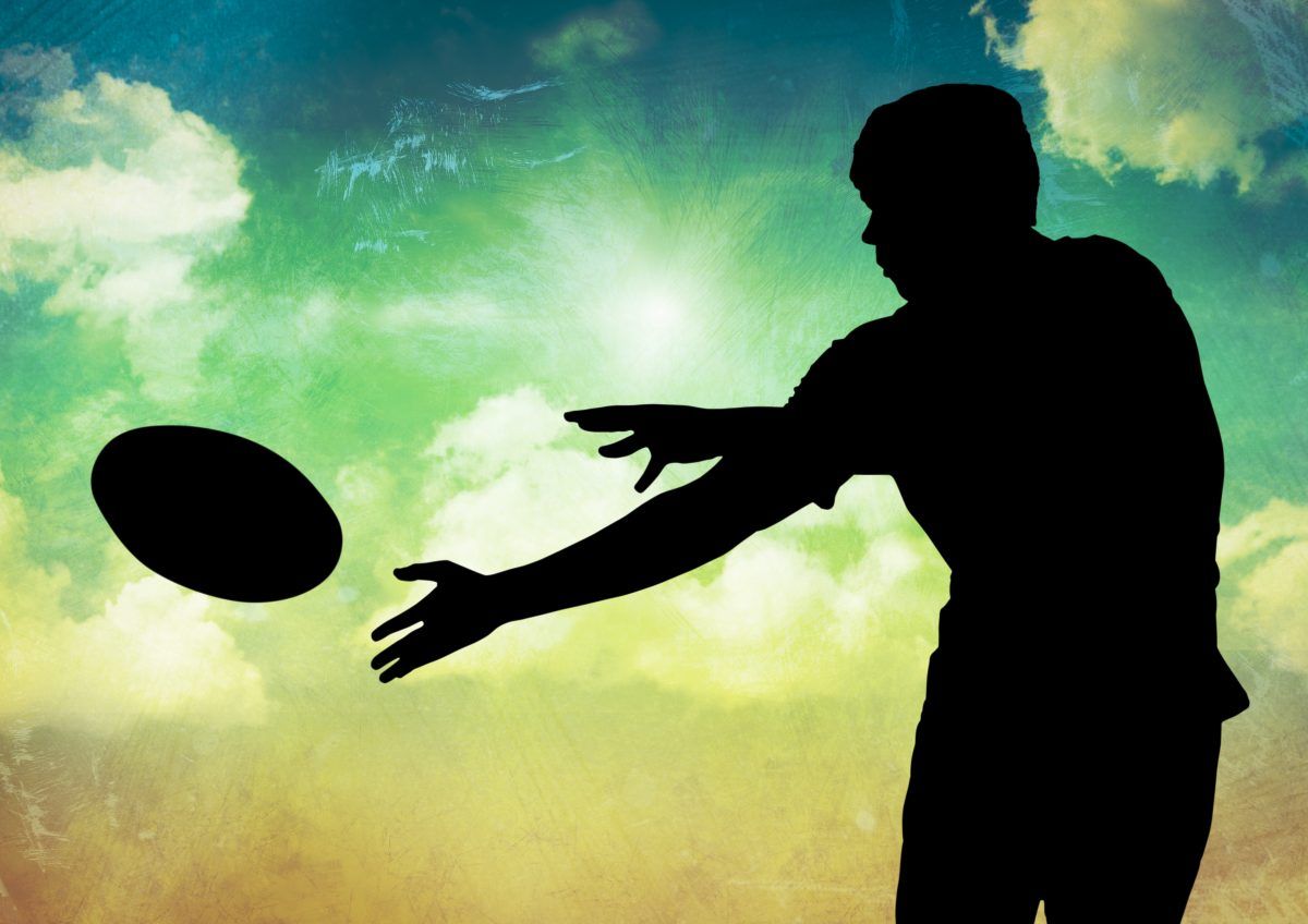 Silhouette of player catching a rugby ball against sky in background